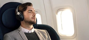    A male on a plane wearing the Sony WH-1000XM3 Headphones looking out of the window